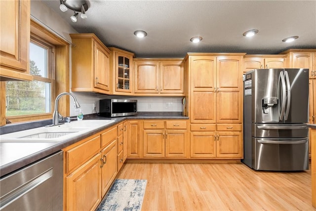 kitchen featuring stainless steel appliances, a sink, light wood-type flooring, glass insert cabinets, and brown cabinets