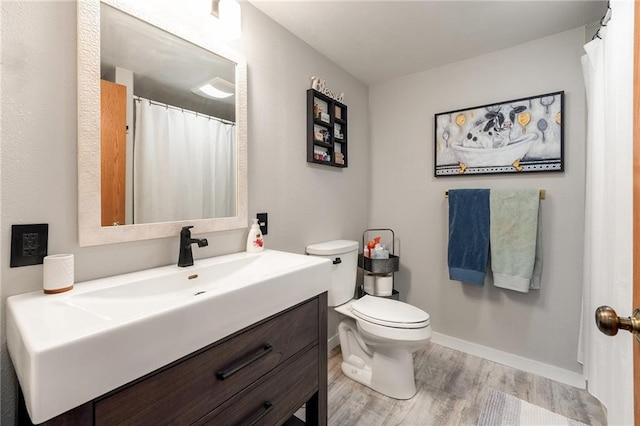 bathroom with wood finished floors, vanity, toilet, and baseboards