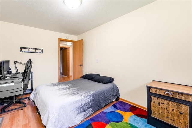 bedroom featuring wood finished floors, baseboards, a textured ceiling, and an office area