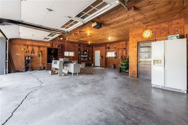 garage with white refrigerator with ice dispenser, wood walls, and a garage door opener
