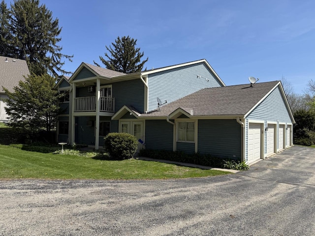 view of front facade with a garage, driveway, a balcony, a front yard, and roof with shingles