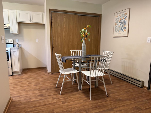 dining room with a baseboard heating unit, wood finished floors, and baseboards