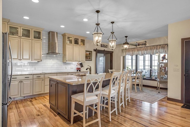 335 Bella Way, Sun Prairie, WI 53590 - kitchen with wall chimney exhaust hood, cream cabinets, freestanding refrigerator, light wood-style flooring, and recessed lighting