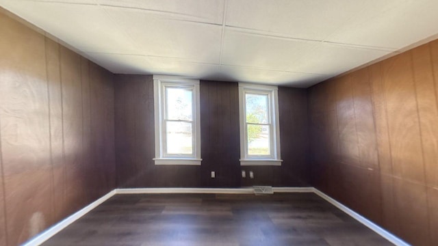 spare room featuring dark wood-type flooring, baseboards, and wood walls