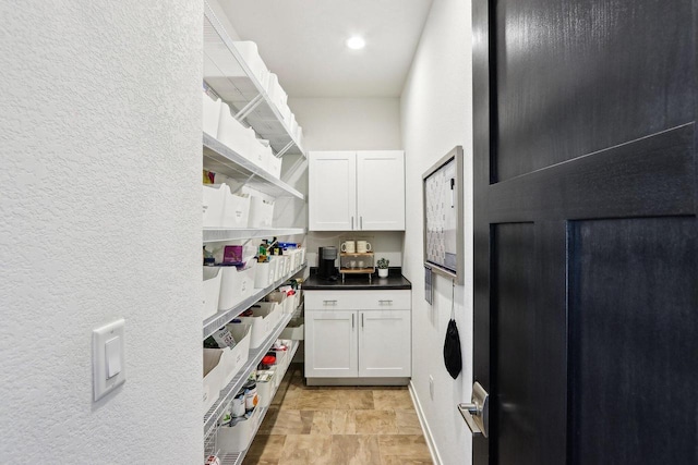 kitchen with open shelves, white cabinetry, dark countertops, and a textured wall