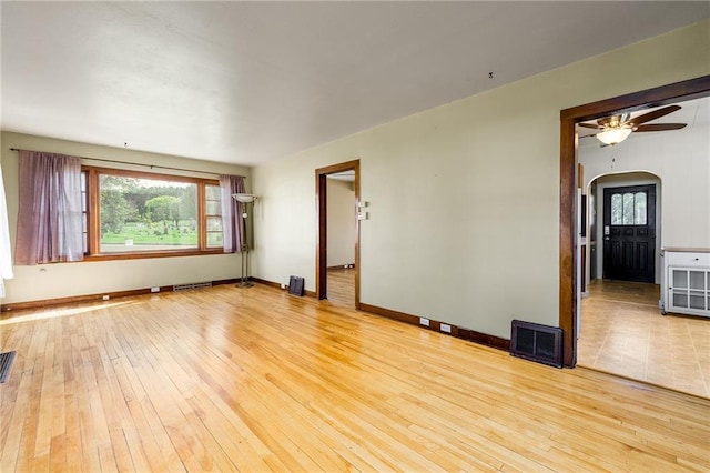 unfurnished room featuring arched walkways, light wood-style flooring, ceiling fan, and baseboards