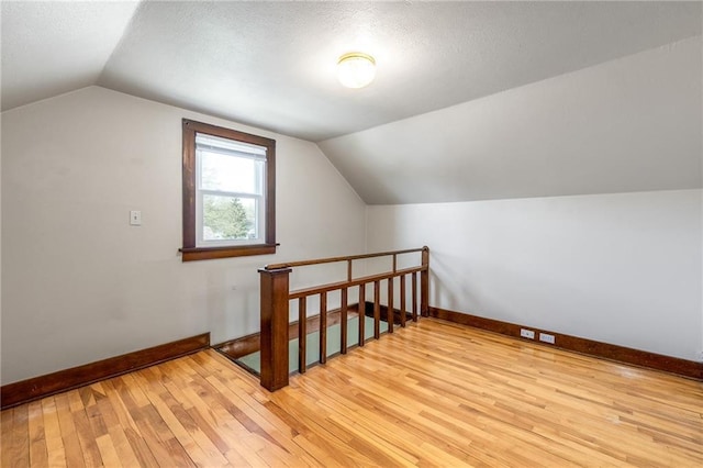 bonus room with baseboards, light wood-style flooring, vaulted ceiling, and a textured ceiling
