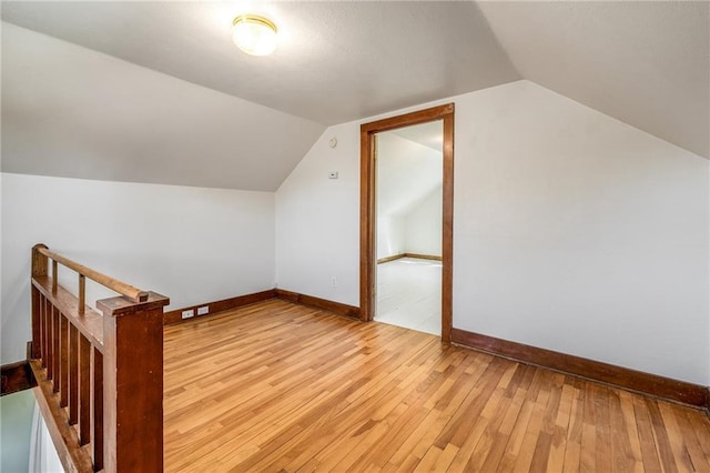 additional living space with light wood-style flooring, lofted ceiling, and baseboards