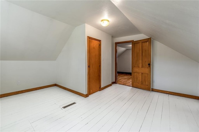 additional living space featuring light wood-style floors, vaulted ceiling, and baseboards