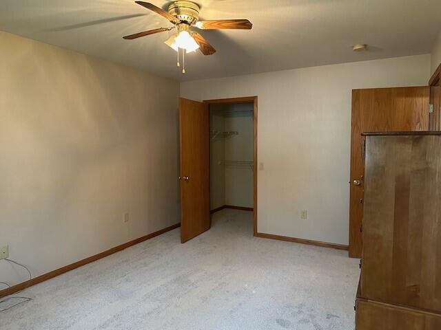 1521 Raveen St, Fort Atkinson, WI 53538 - unfurnished bedroom with light colored carpet, baseboards, a walk in closet, and a ceiling fan