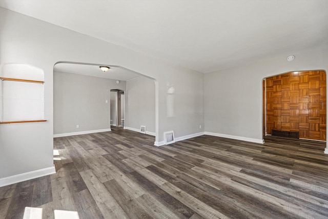 spare room with arched walkways, wood finished floors, and baseboards