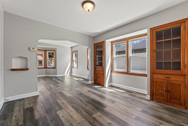 unfurnished dining area featuring arched walkways, plenty of natural light, dark wood-style flooring, and baseboards