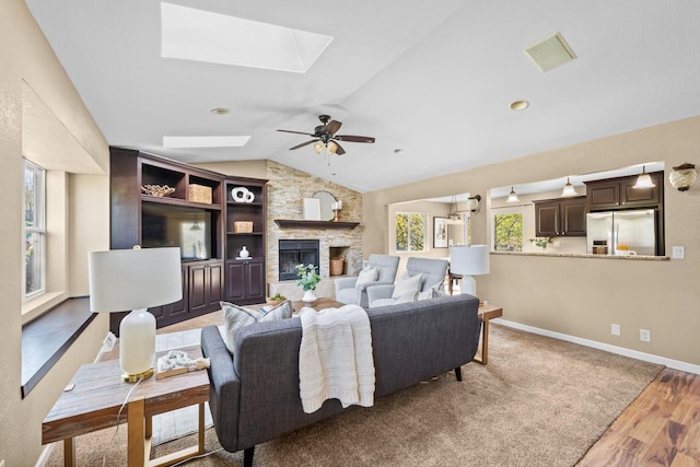 252 Willow Dr, Hartland, WI 53029 - living room featuring a skylight, a ceiling fan, vaulted ceiling, a stone fireplace, and wood finished floors