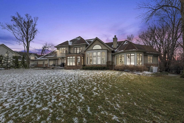536 Sunrise Bay Rd, Neenah, WI 54956 - back of house at dusk with a chimney, a balcony, brick siding, and a lawn