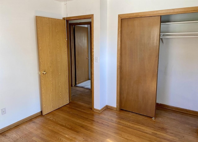 unfurnished bedroom featuring wood finished floors, a closet, and baseboards