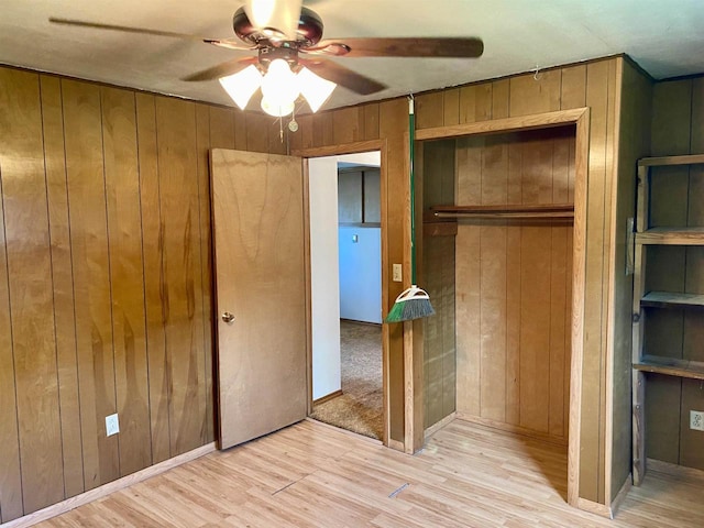 unfurnished bedroom with wooden walls, light wood-style flooring, a closet, and a ceiling fan
