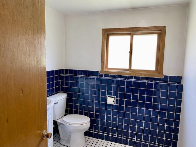 bathroom with toilet, tile patterned flooring, tile walls, and wainscoting