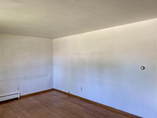 empty room with wood finished floors, baseboards, and baseboard heating