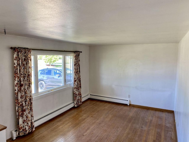 empty room featuring wood finished floors, a baseboard heating unit, and baseboards