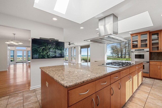 7515 N Beach Dr, Fox Point, WI 53217 - kitchen with island exhaust hood, appliances with stainless steel finishes, a skylight, light tile patterned floors, and backsplash