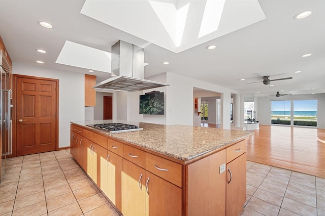 7515 N Beach Dr, Fox Point, WI 53217 - kitchen with island range hood, a skylight, light tile patterned floors, stainless steel gas stovetop, and light stone countertops