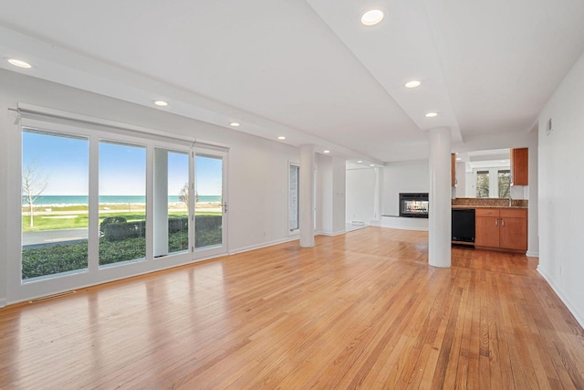 7515 N Beach Dr, Fox Point, WI 53217 - unfurnished living room featuring recessed lighting, light wood finished floors, a multi sided fireplace, baseboards, and a water view