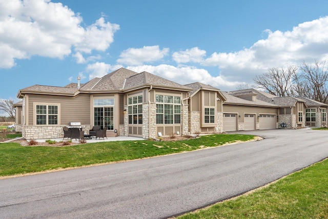 W139S9977 Jay Dr, Muskego, WI 53150 - exterior space featuring stone siding, an attached garage, a lawn, asphalt driveway, and a patio