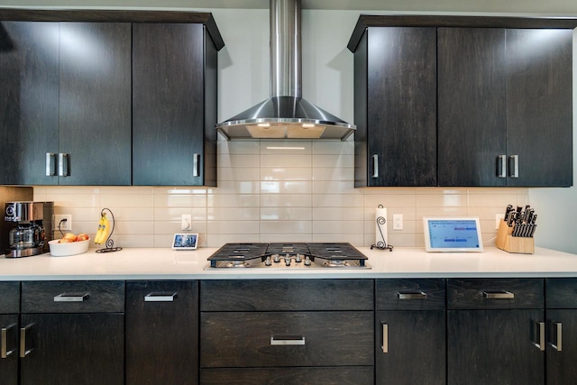 kitchen with wall chimney range hood, stainless steel gas cooktop, light countertops, and backsplash