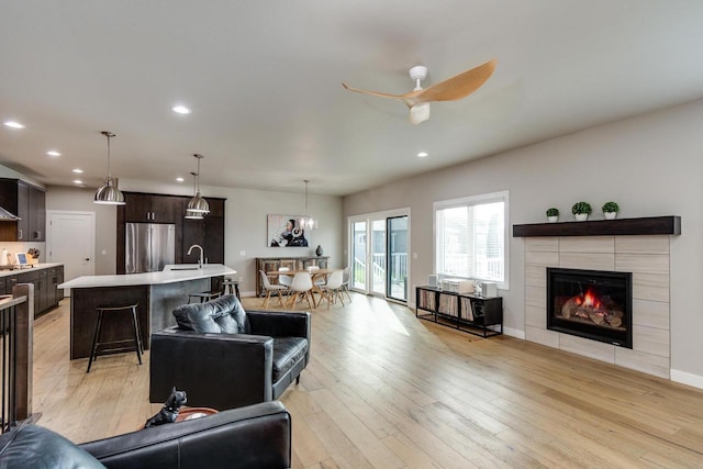 living room featuring light wood-style floors, recessed lighting, ceiling fan, a fireplace, and baseboards