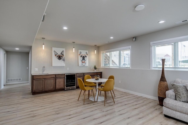 dining space with beverage cooler, light wood-style flooring, recessed lighting, baseboards, and bar