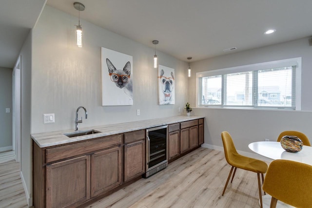 kitchen with beverage cooler, a sink, light wood-style flooring, baseboards, and decorative light fixtures