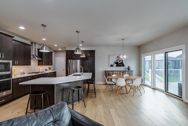 kitchen with appliances with stainless steel finishes, wall chimney exhaust hood, light countertops, light wood finished floors, and recessed lighting