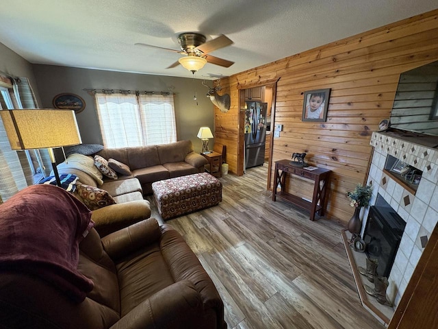 121 W Clark St, Plainfield, WI 54966 - living room featuring a ceiling fan, wooden walls, a tiled fireplace, light wood-type flooring, and a textured ceiling