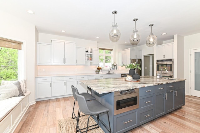7601 S Cambridge Dr, Franklin, WI 53132 - kitchen featuring white cabinetry, appliances with stainless steel finishes, light wood-style floors, open shelves, and a breakfast bar