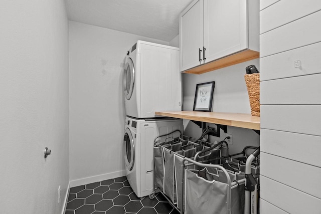 laundry room with cabinet space, stacked washer / drying machine, dark tile patterned floors, baseboards, and a desk