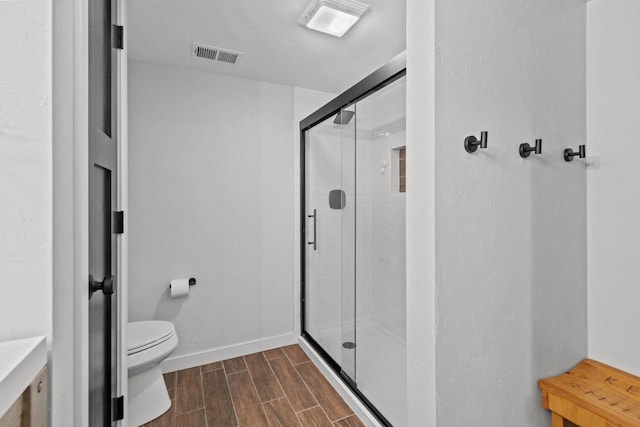 bathroom featuring wood finish floors, a shower stall, toilet, and baseboards