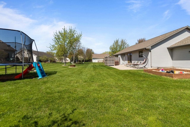 view of green lawn with a trampoline and a patio area