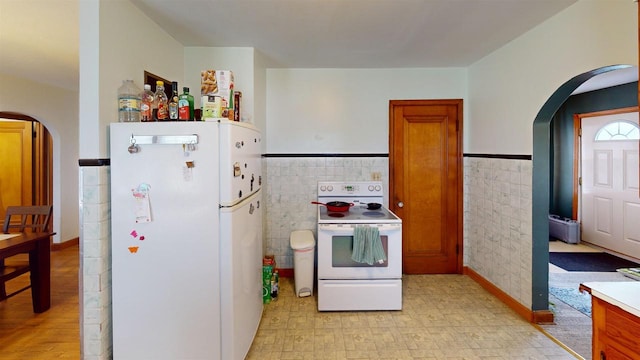 5869 State Highway 27, Sparta, WI 54656 - kitchen with white appliances, arched walkways, tile walls, a wainscoted wall, and brown cabinetry