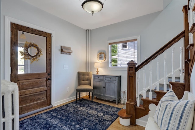 entrance foyer featuring wood finished floors, stairway, radiator heating unit, and baseboards