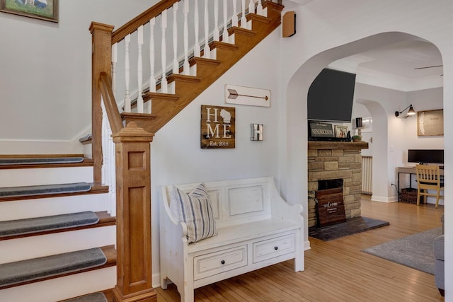 stairway featuring wood-type flooring, a stone fireplace, and arched walkways