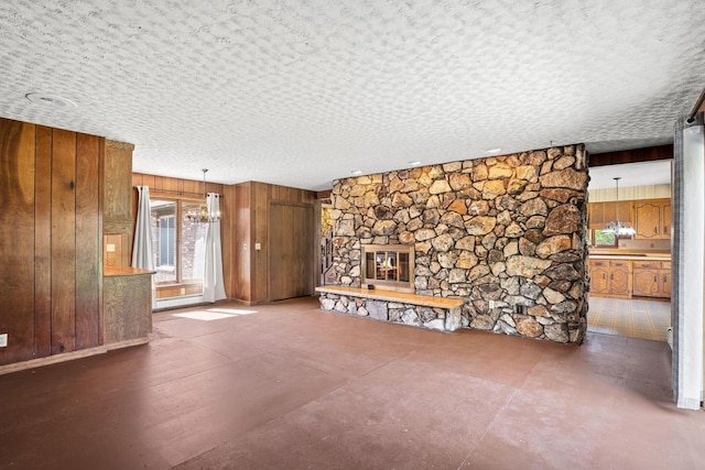 9 Sandalwood Ct, Wind Point, WI 53402 - unfurnished living room featuring wooden walls, a fireplace, a chandelier, concrete flooring, and a textured ceiling