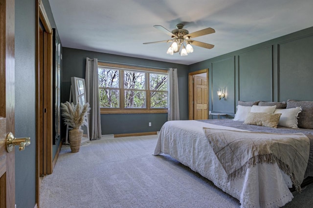 bedroom with light colored carpet, ceiling fan, a decorative wall, and baseboards