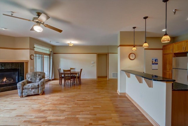 6767 Frank Lloyd Wright Ave Unit 219, Middleton, WI 53562 - kitchen featuring freestanding refrigerator, light wood finished floors, a ceiling fan, a tile fireplace, and a breakfast bar