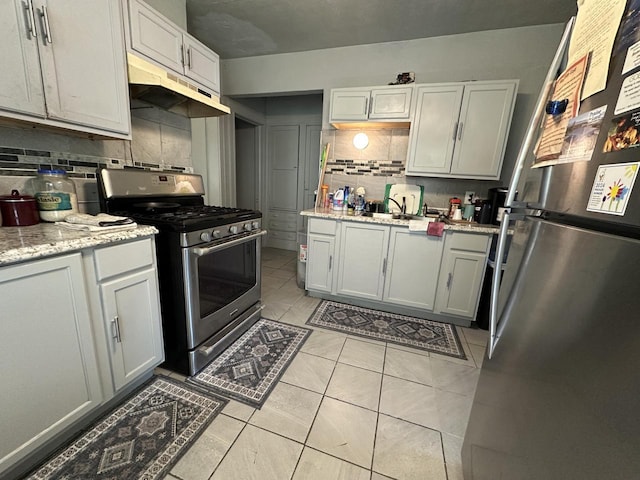 kitchen with appliances with stainless steel finishes, under cabinet range hood, backsplash, light tile patterned floors, and light stone counters