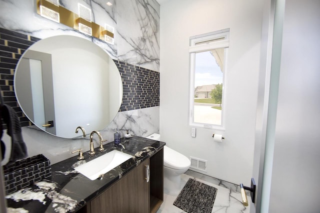 half bathroom with marble look tile flooring, tile walls, toilet, and vanity