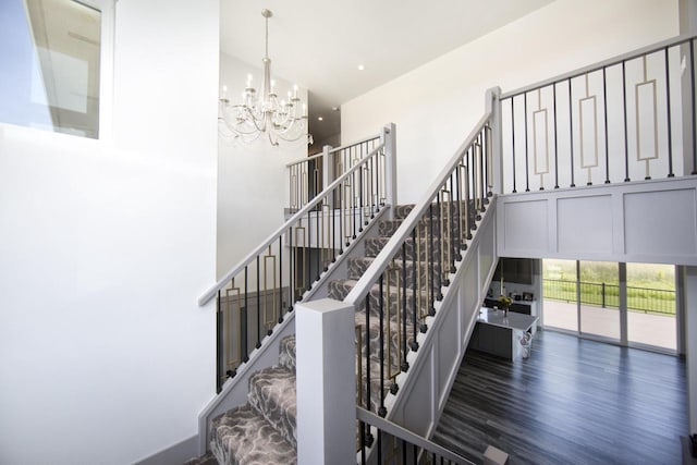 stairway with a towering ceiling, a chandelier, and wood finished floors