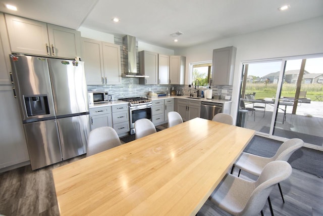 kitchen featuring appliances with stainless steel finishes, wall chimney exhaust hood, gray cabinetry, dark wood finished floors, and decorative backsplash