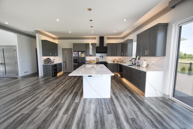 kitchen featuring black appliances, wall chimney range hood, a sink, light stone counters, and a kitchen island