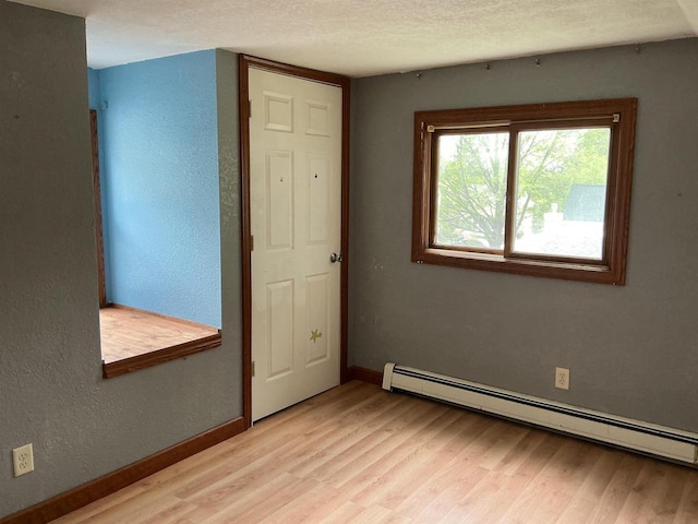 empty room featuring baseboard heating, light wood finished floors, a textured wall, baseboards, and a textured ceiling