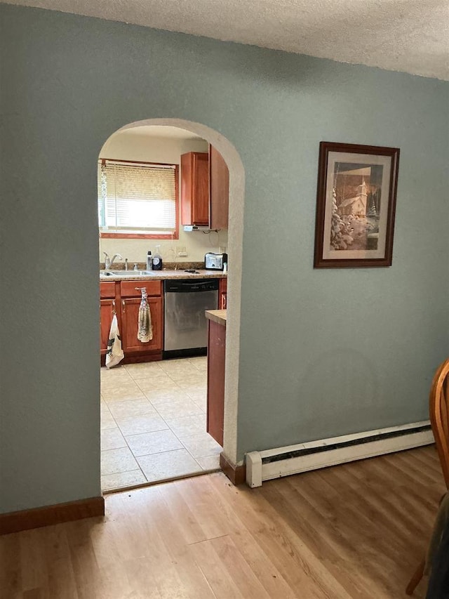corridor with baseboard heating, arched walkways, a sink, baseboards, and light wood finished floors